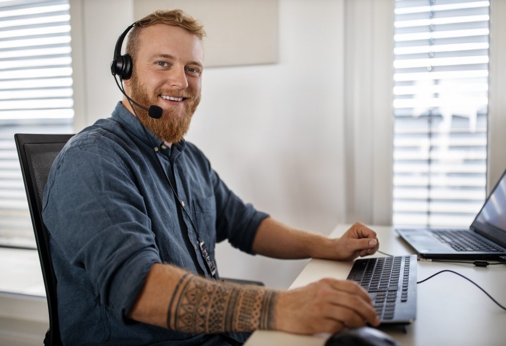 Man working in a customer service industry. Smiling businessman in casuals wearing headset sitting at his desk and looking at camera.