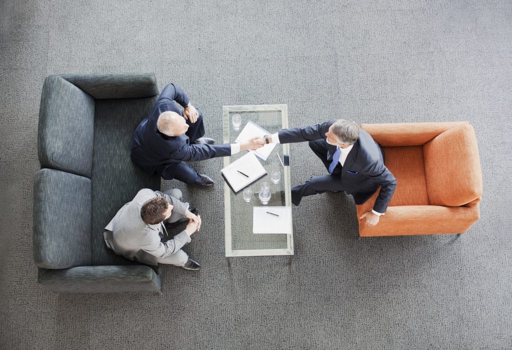 Businessmen shaking hands across coffee table in office lobby
