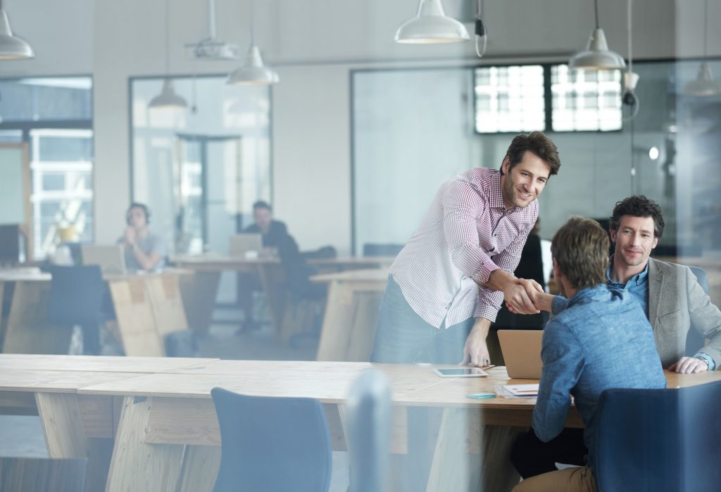 Shot of two coworkers shaking hands at a table in an office