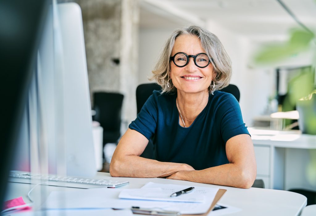 Portrait of confident mature businesswoman. Smiling female professional is working in creative office. She is wearing eyeglasses.